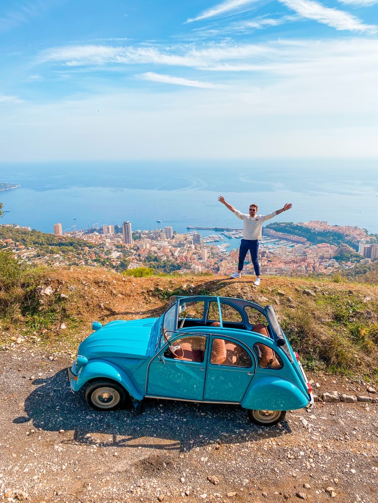 Man standing on Tête de Chien Mountain with blue car above Monaco on French Riviera
